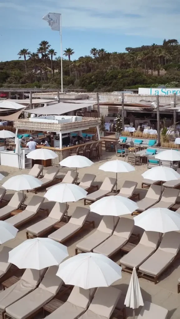 Elevated view of the bar, sunbeds and white parasols with the La Serena flag at Plage La Serena Ramatuelle Saint-Tropez