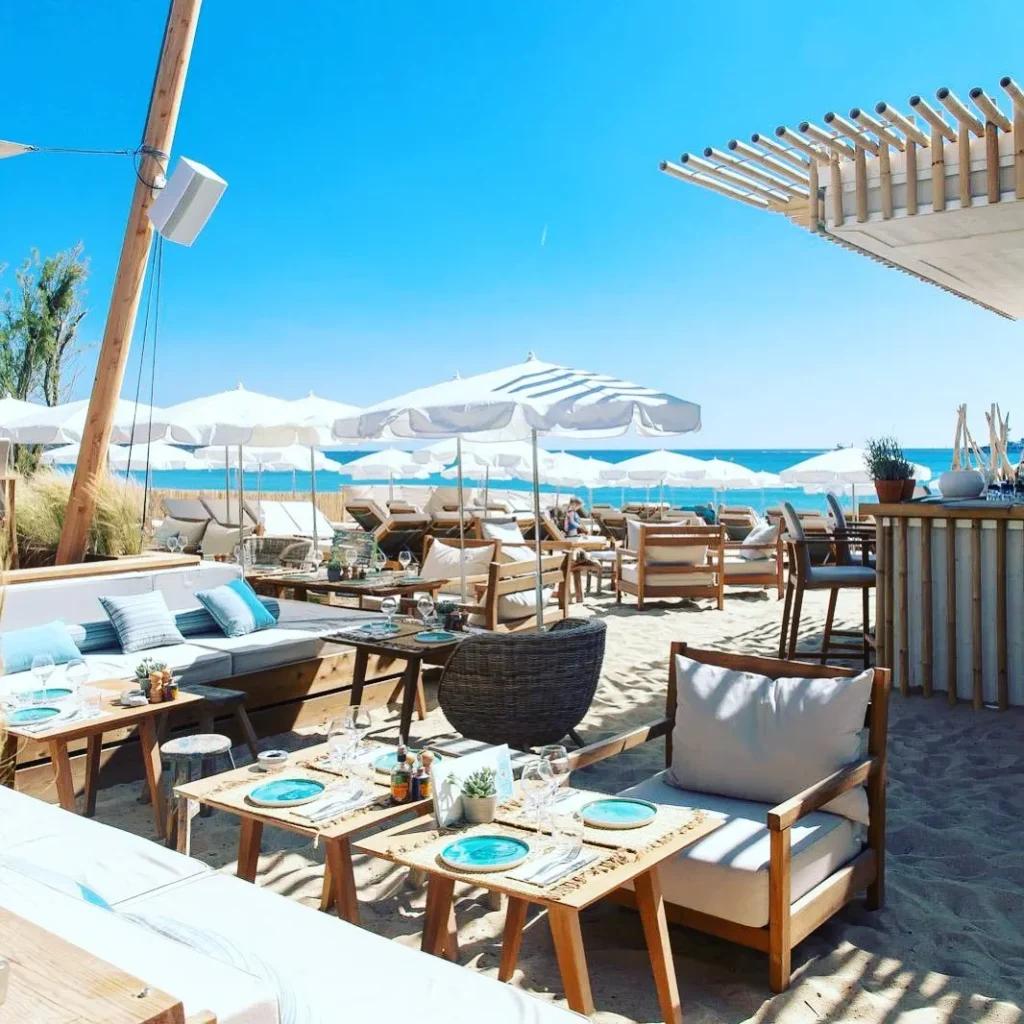 Beach lounge with low sofas, set tables and parasols on the sand at Plage La Serena Ramatuelle Saint-Tropez