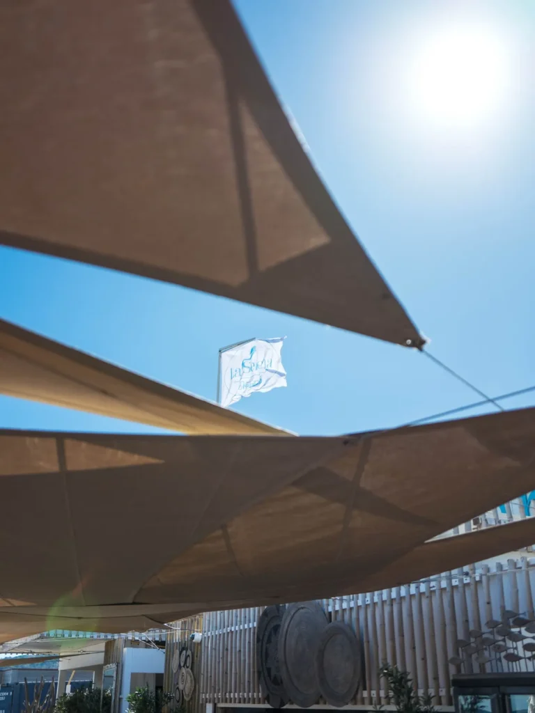 La Serena flag flying above the sail canopies against a blue sky at Plage La Serena Ramatuelle Saint-Tropez