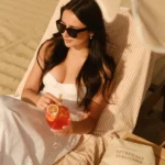 Guest in a white dress relaxing on a striped sunbed with a cocktail at Plage La Serena Ramatuelle Saint-Tropez