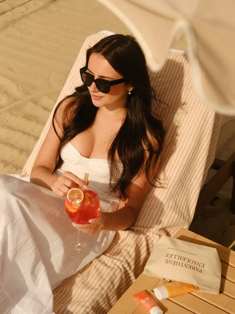 Guest in a white dress relaxing on a striped sunbed with a cocktail at Plage La Serena Ramatuelle Saint-Tropez
