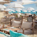 Restaurant tables and cushioned daybeds among white parasols by the sea at Plage La Serena Ramatuelle Saint-Tropez