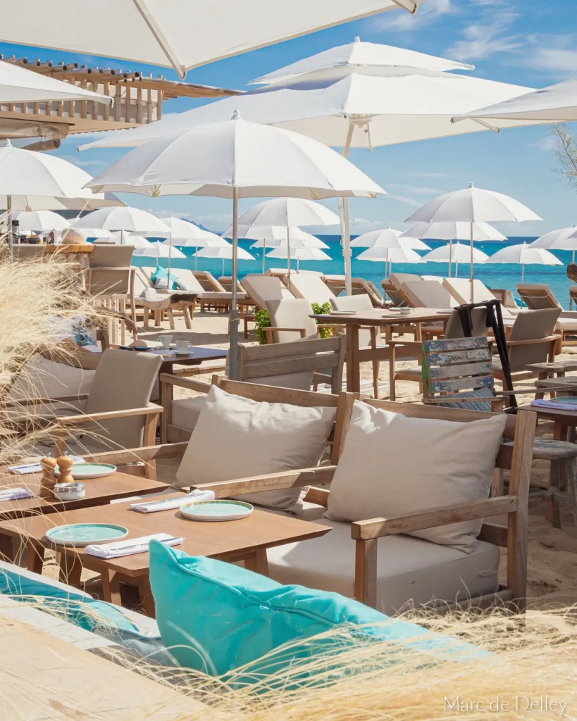 Restaurant tables and cushioned daybeds among white parasols by the sea at Plage La Serena Ramatuelle Saint-Tropez