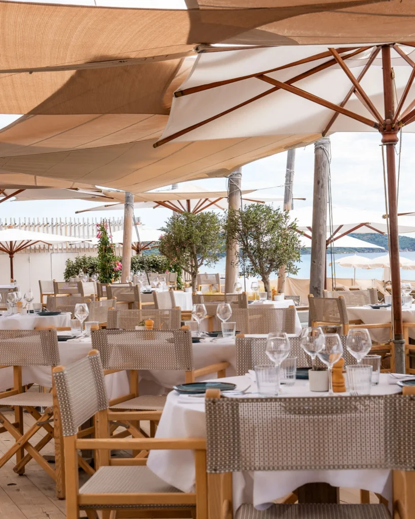 Restaurant tables under wooden parasols and olive trees with a sea view at Plage La Serena Ramatuelle Saint-Tropez