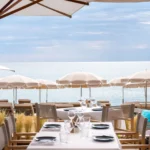 Set restaurant tables with white parasols and an open sea view at Plage La Serena Ramatuelle Saint-Tropez