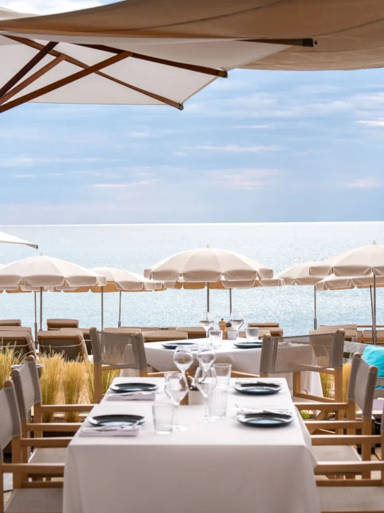 Set restaurant tables with white parasols and an open sea view at Plage La Serena Ramatuelle Saint-Tropez