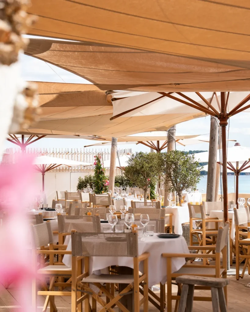 Restaurant tables beneath sail shades and parasols by the beach at Plage La Serena Ramatuelle Saint-Tropez