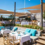 Beach restaurant with turquoise banquette cushions and sail canopies below the La Serena flag at Plage La Serena Ramatuelle Saint-Tropez
