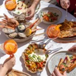 Shared spread of seafood, burrata and spritzes on a beachside table at Plage La Serena Ramatuelle Saint-Tropez