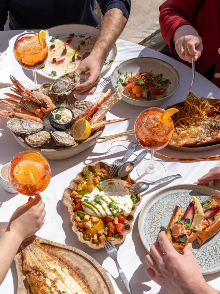 Shared spread of seafood, burrata and spritzes on a beachside table at Plage La Serena Ramatuelle Saint-Tropez
