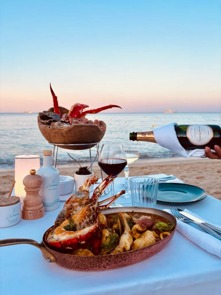 Seafood platter and lobster pan with champagne poured at a beachside table at dusk at Plage La Serena Ramatuelle Saint-Tropez