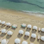 Overhead view of white parasols and sunbeds beside turquoise water at Plage La Serena Ramatuelle Saint-Tropez