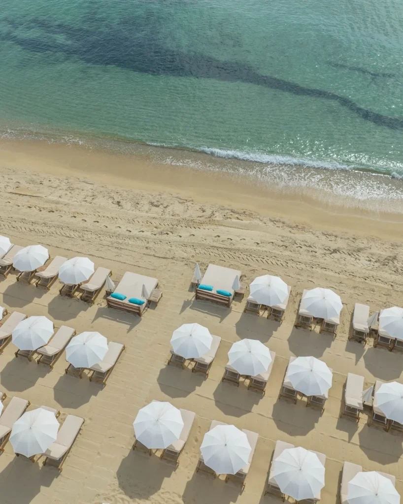 Overhead view of white parasols and sunbeds beside turquoise water at Plage La Serena Ramatuelle Saint-Tropez