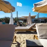 Sunbeds and parasols on the sand with the La Serena flag flying beyond at Plage La Serena Ramatuelle Saint-Tropez
