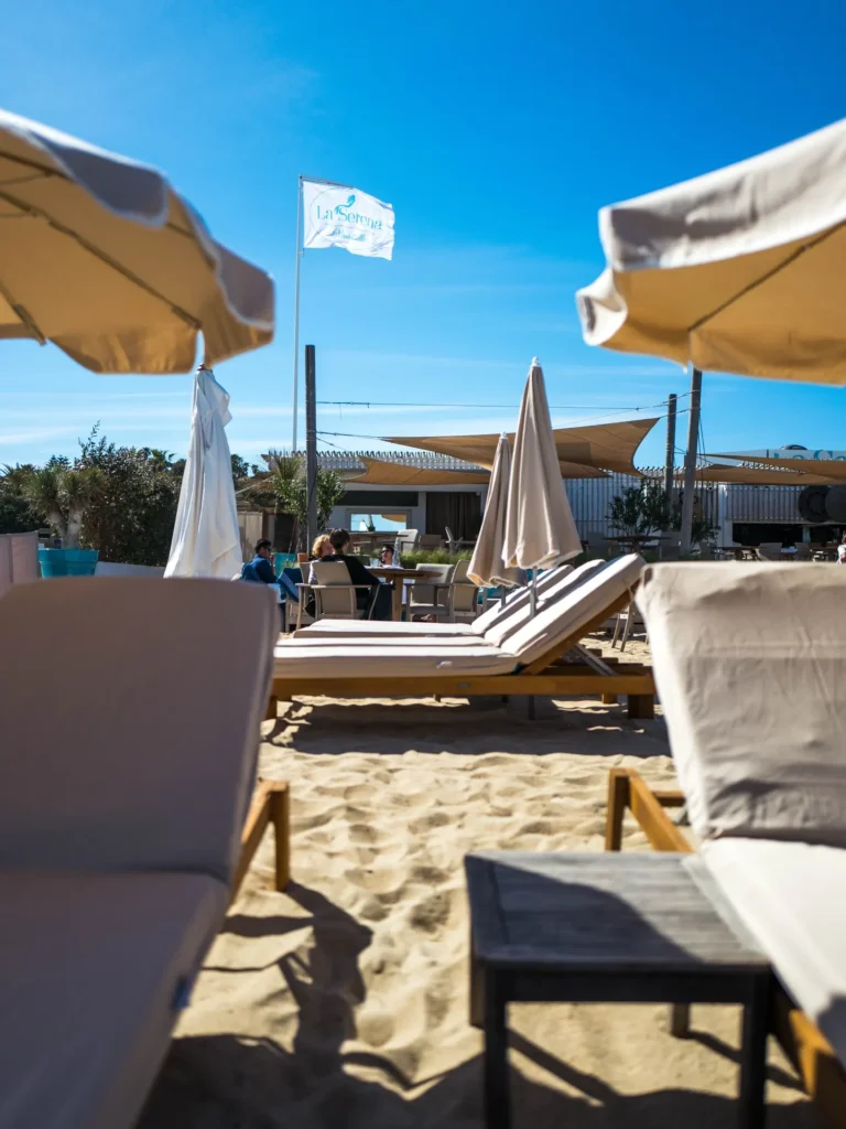 Sunbeds and parasols on the sand with the La Serena flag flying beyond at Plage La Serena Ramatuelle Saint-Tropez