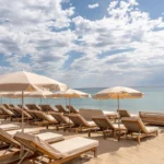 Cream sunbeds and parasols on the sand under a cloud-streaked sky at Plage La Serena Ramatuelle Saint-Tropez