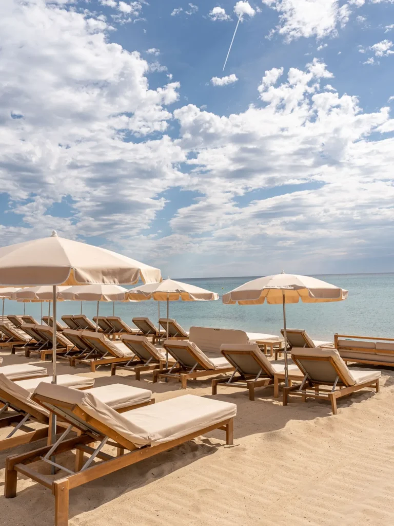 Cream sunbeds and parasols on the sand under a cloud-streaked sky at Plage La Serena Ramatuelle Saint-Tropez