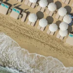 Overhead view of white parasols and sunbeds meeting the breaking waves at Plage La Serena Ramatuelle Saint-Tropez