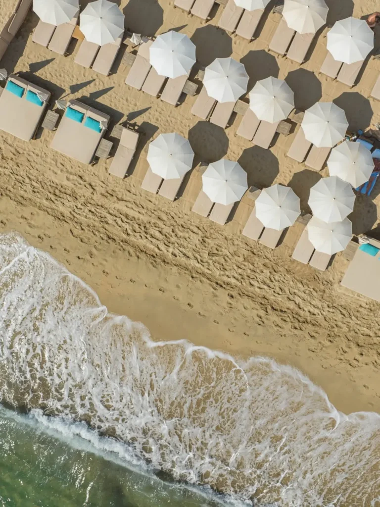 Overhead view of white parasols and sunbeds meeting the breaking waves at Plage La Serena Ramatuelle Saint-Tropez