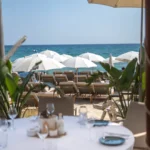 Set table framed by greenery overlooking sunbeds and the sea at Plage La Serena Ramatuelle Saint-Tropez