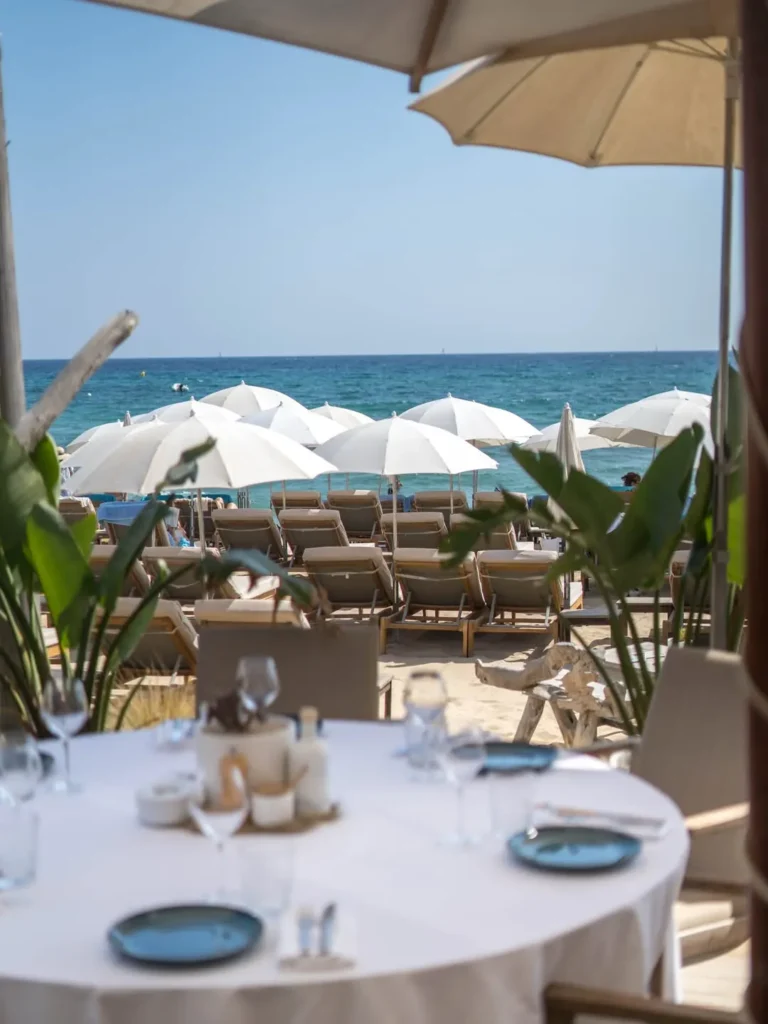 Set table framed by greenery overlooking sunbeds and the sea at Plage La Serena Ramatuelle Saint-Tropez