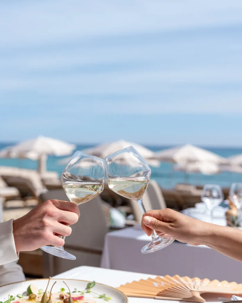 Two guests toasting with white wine over a sea view at Plage La Serena Ramatuelle Saint-Tropez