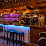 Bartender preparing a drink behind the tiled bar with backlit bottles and stools at Restaurante El Cuerno Palma