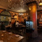 Dining room with a crystal chandelier, gilded bull skull and mounted stag on ochre walls at Restaurante El Cuerno Palma