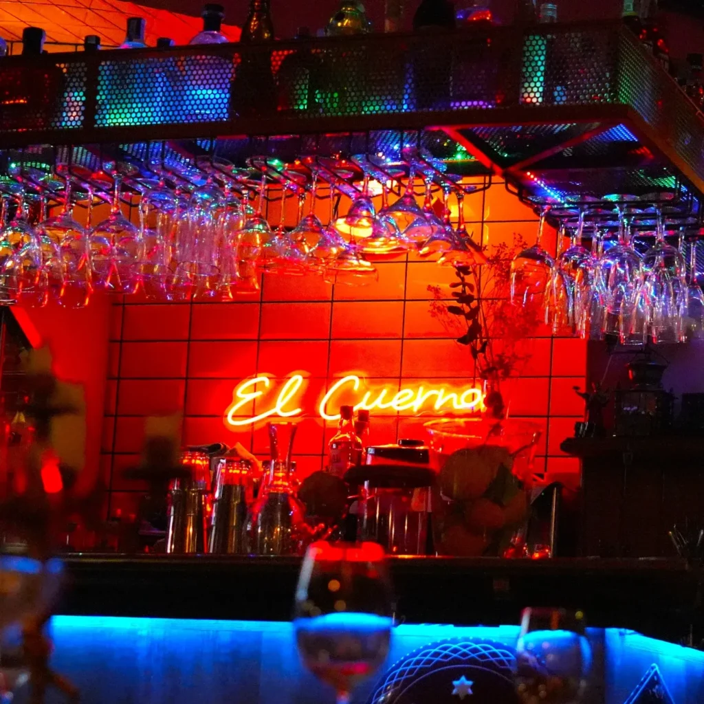 El Cuerno neon sign glowing behind the bar under rows of hanging glasses at Restaurante El Cuerno Palma