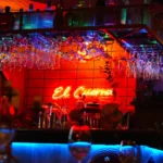 El Cuerno neon sign glowing behind the bar under rows of hanging glasses at Restaurante El Cuerno Palma