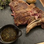 Sliced grilled chuletón steak with potato and a herb sauce on a slate board at Restaurante El Cuerno Palma