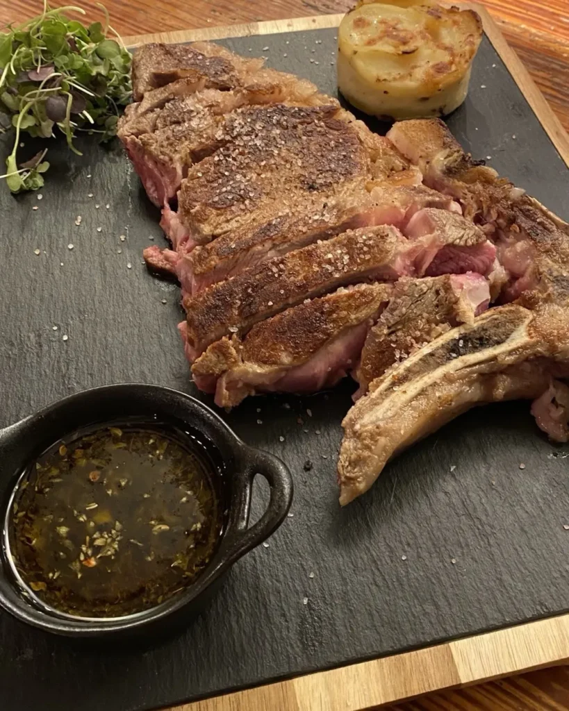 Sliced grilled chuletón steak with potato and a herb sauce on a slate board at Restaurante El Cuerno Palma