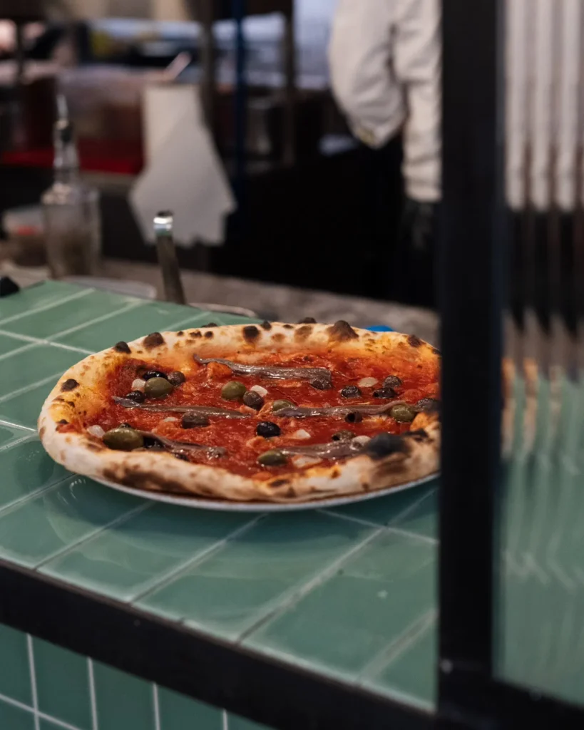 Wood-fired pizza with anchovies and olives at the pass on a green-tiled counter at Rikito Palma