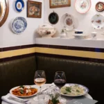 Corner banquette with pasta, ravioli and wine below a plate-covered wall at Rikito Palma