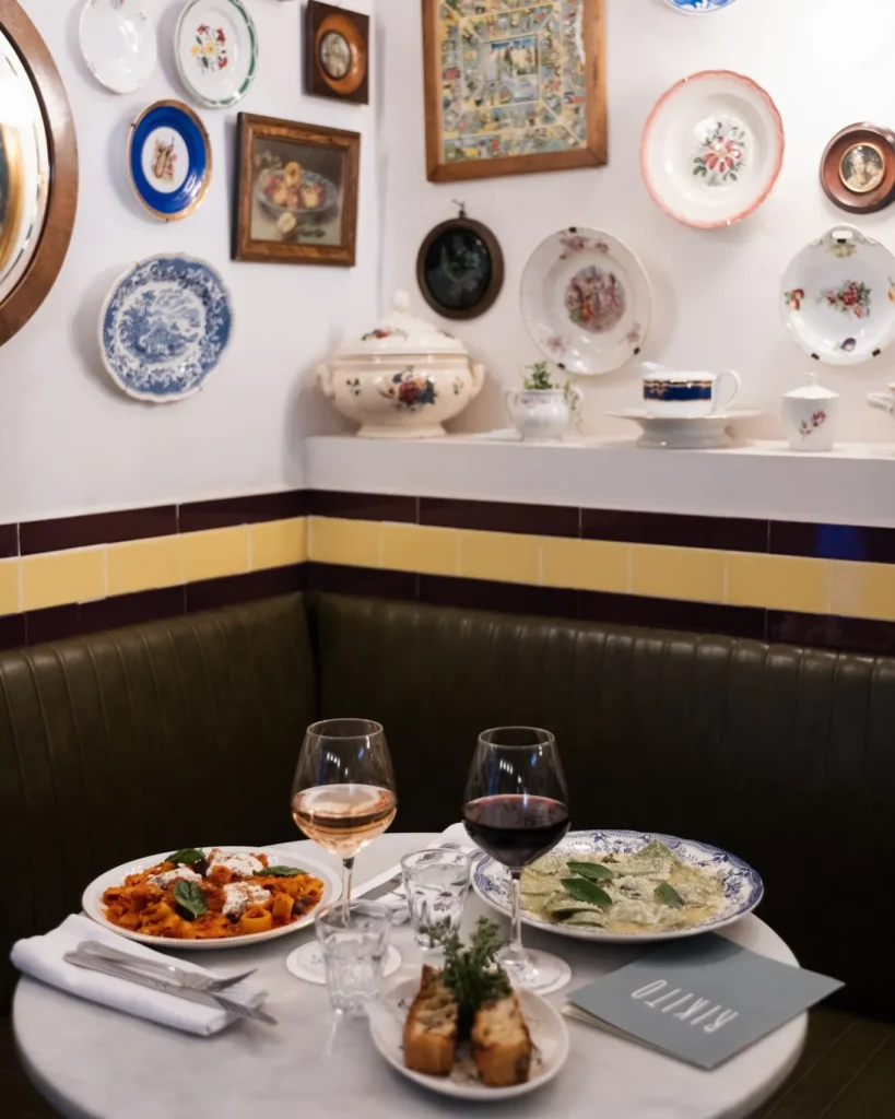 Corner banquette with pasta, ravioli and wine below a plate-covered wall at Rikito Palma