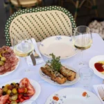 Charcuterie, tomato salad and toasts with white wine on a terrace table at Rikito Palma