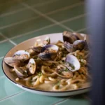 Pasta with clams and parsley in a bowl on a green-tiled surface at Rikito Palma