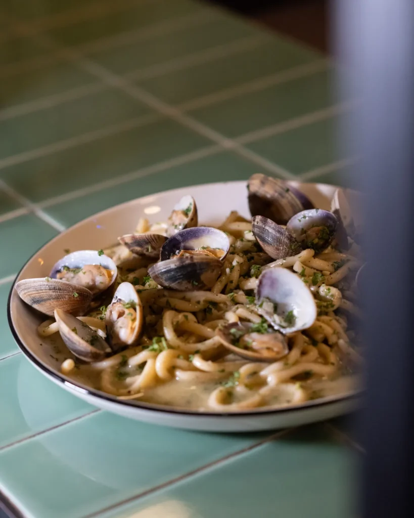 Pasta with clams and parsley in a bowl on a green-tiled surface at Rikito Palma