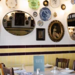 Interior table set against yellow tiles and a wall of plates and mirrors at Rikito Palma