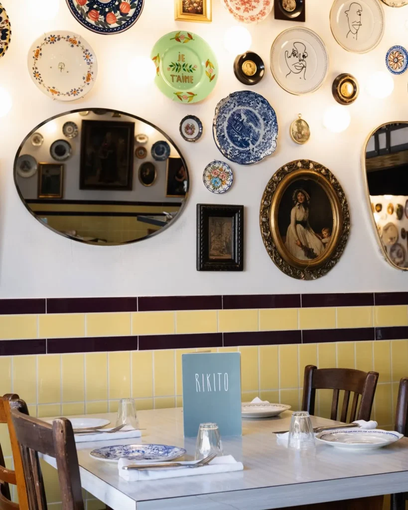 Interior table set against yellow tiles and a wall of plates and mirrors at Rikito Palma