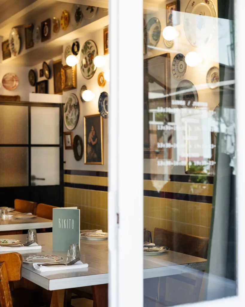 View through the window into the plate-lined dining room with a Rikito menu on the table at Rikito Palma