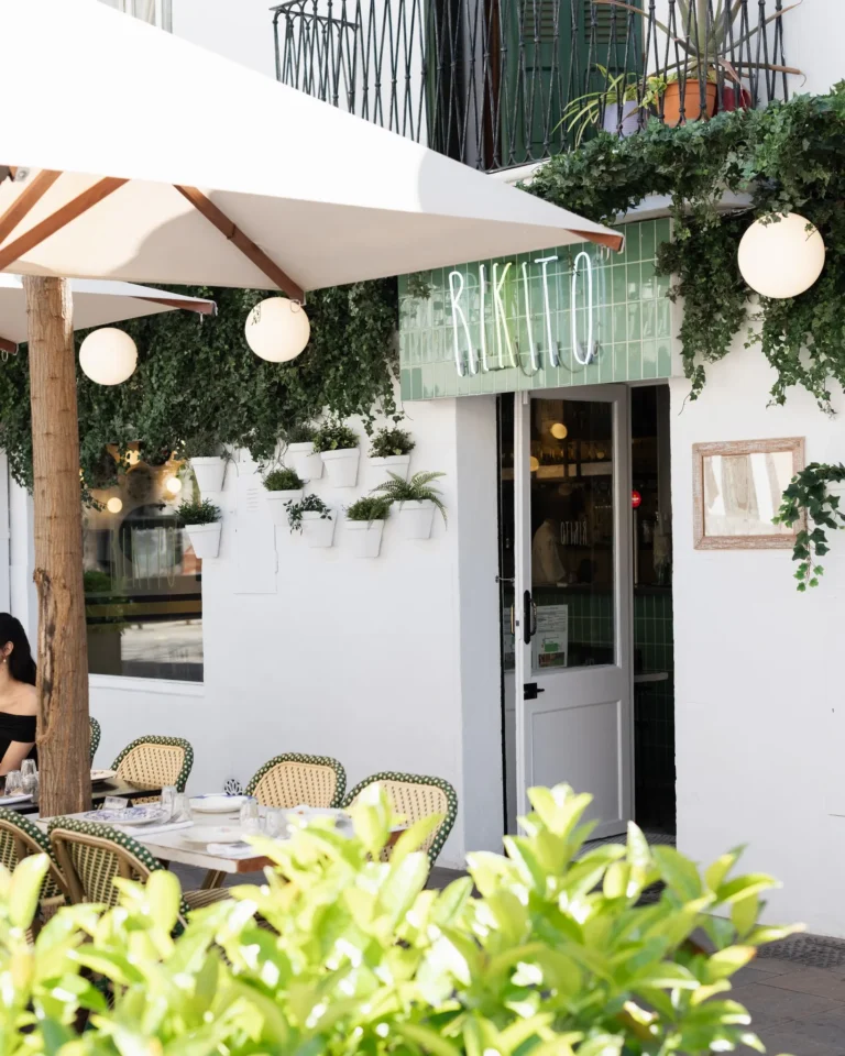 Green-tiled Rikito neon storefront with a shaded terrace and bistro chairs at Rikito Palma