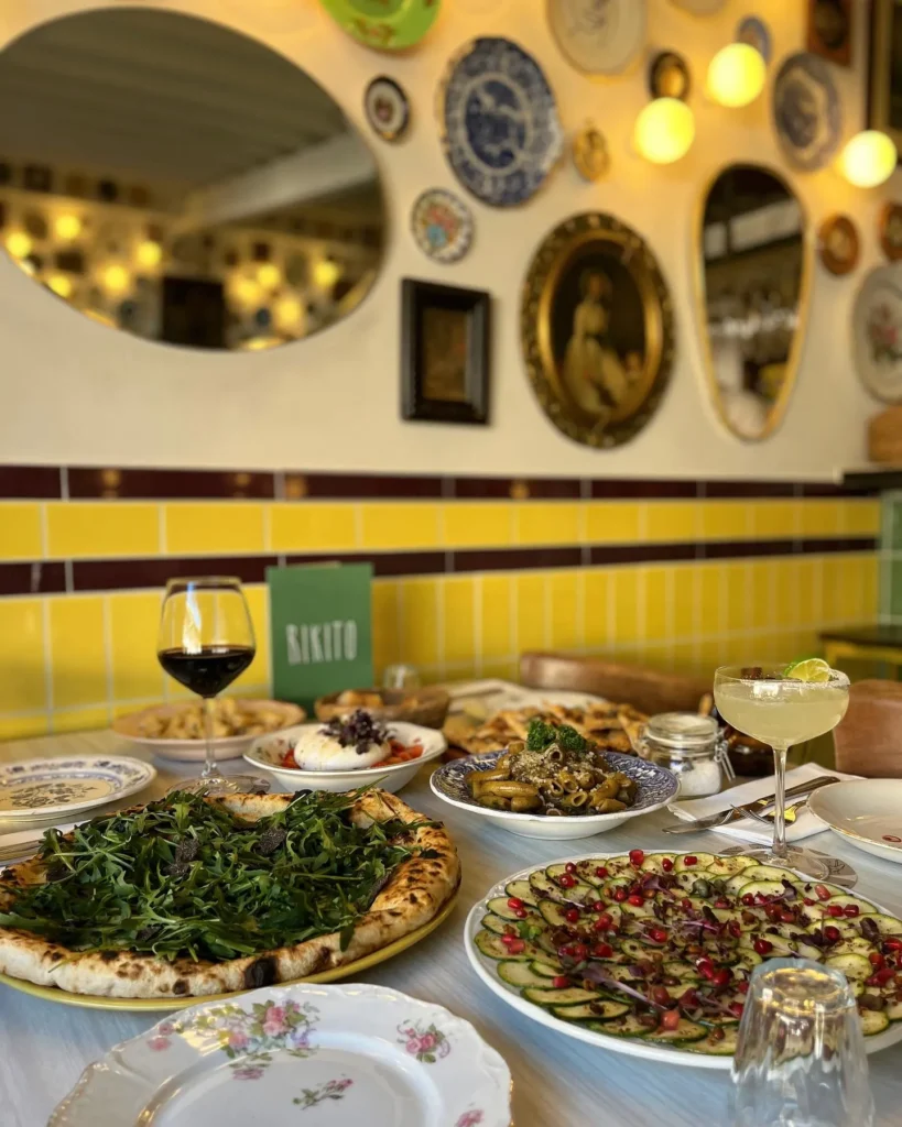 Spread of pizza, courgette carpaccio and cocktails below the plate wall at Rikito Palma