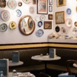 Green leather banquette and marble tables beneath a gallery of vintage plates at Rikito Palma