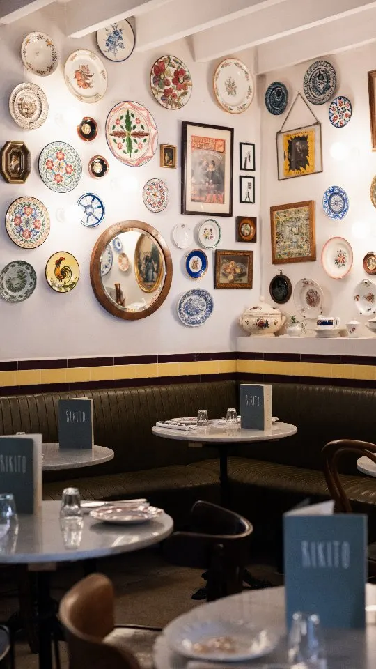 Green leather banquette and marble tables beneath a gallery of vintage plates at Rikito Palma