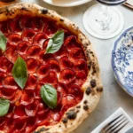 Wood-fired pepperoni pizza with basil on a marble table at Rikito Palma