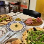 Pizzas, gnocchi and salami shared across a table with red wine at Rikito Palma