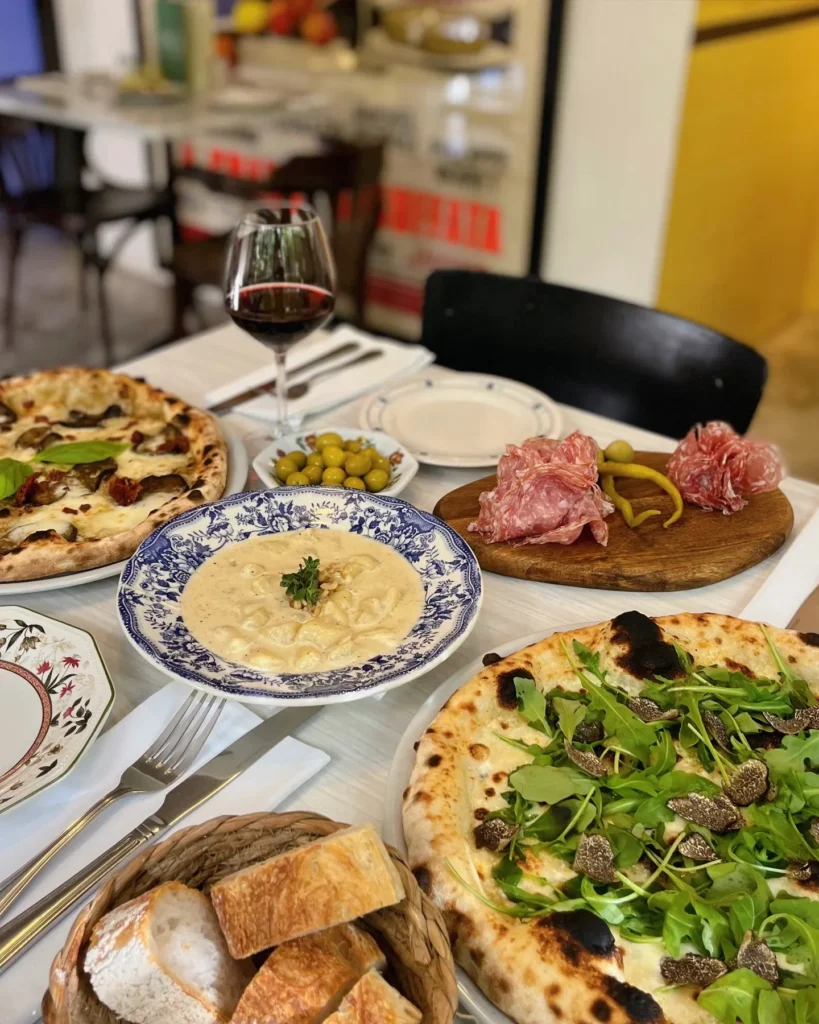 Pizzas, gnocchi and salami shared across a table with red wine at Rikito Palma