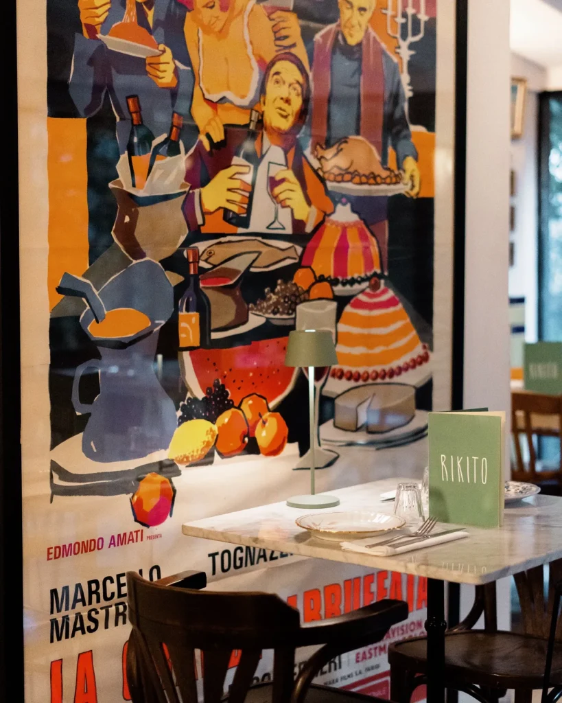 Marble table with a Rikito menu beside a vintage Italian film poster at Rikito Palma