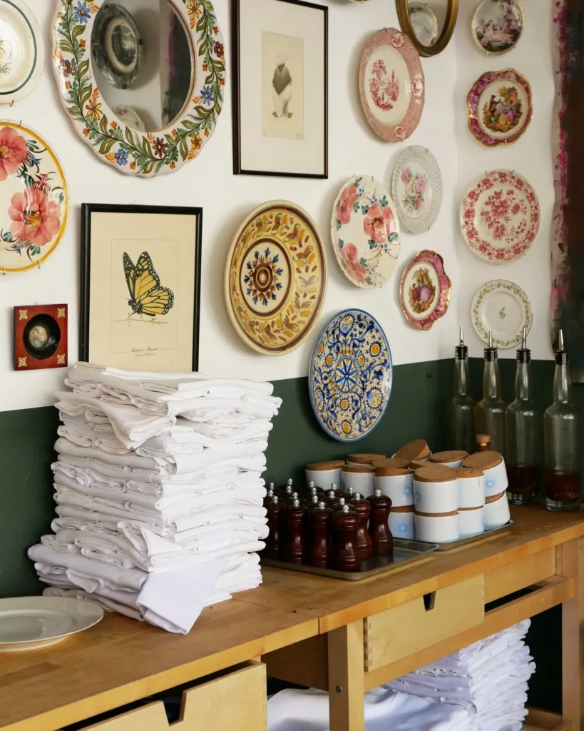 Service station with stacked napkins and pepper mills beneath a wall of decorative plates at Rikito Palma
